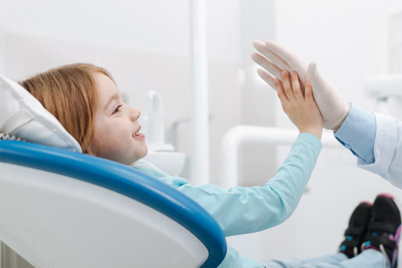 Familiäre Atmosphäre in der Zahnarztpraxis Kind im Behandlungsstuhl gibt dem Zahnarzt ein High Five